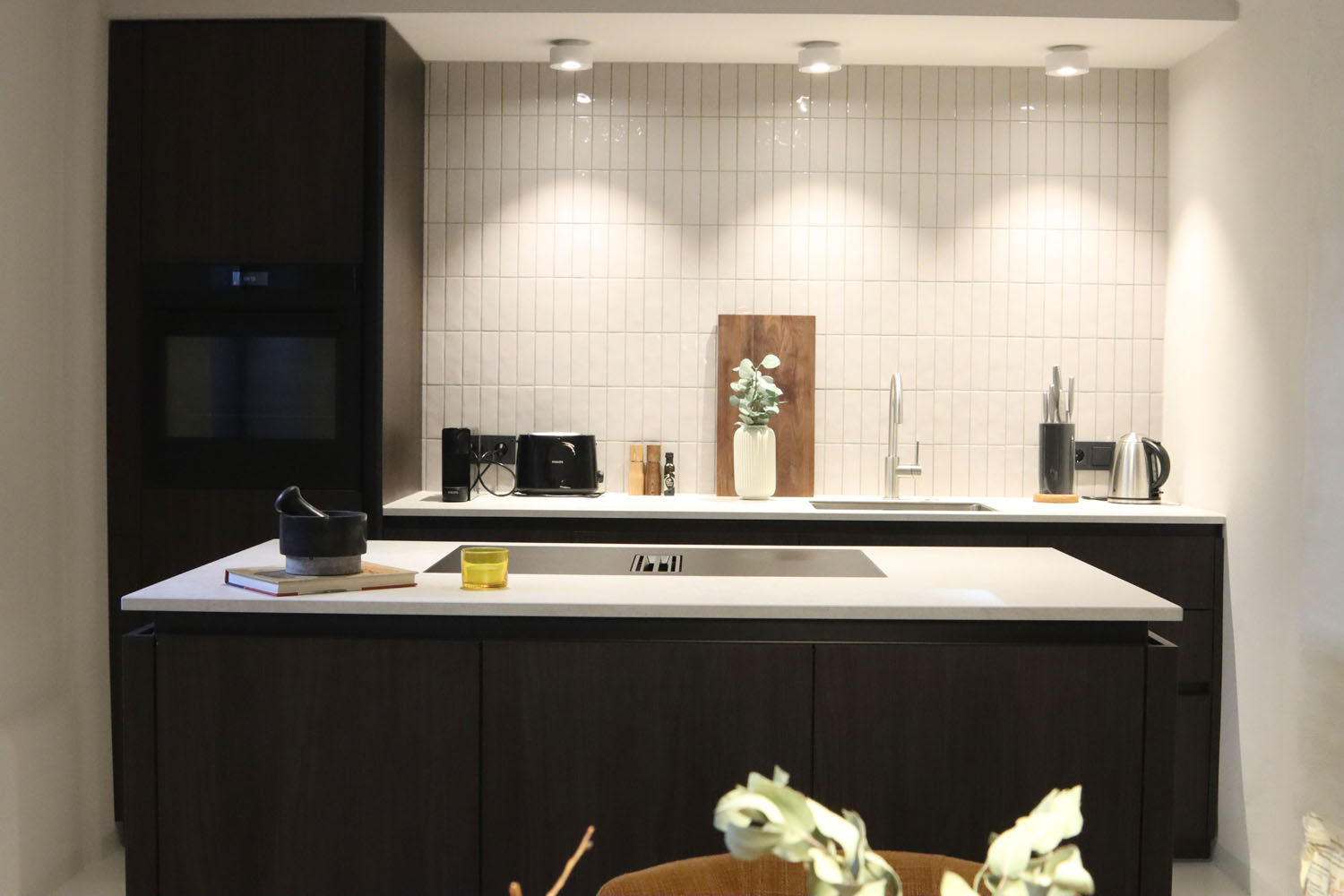 Moderne Küche mit dunklen Schränken, heller Arbeitsplatte, eingebautem Ofen und stilvoller Beleuchtung. Dekoration ist minimalistisch.