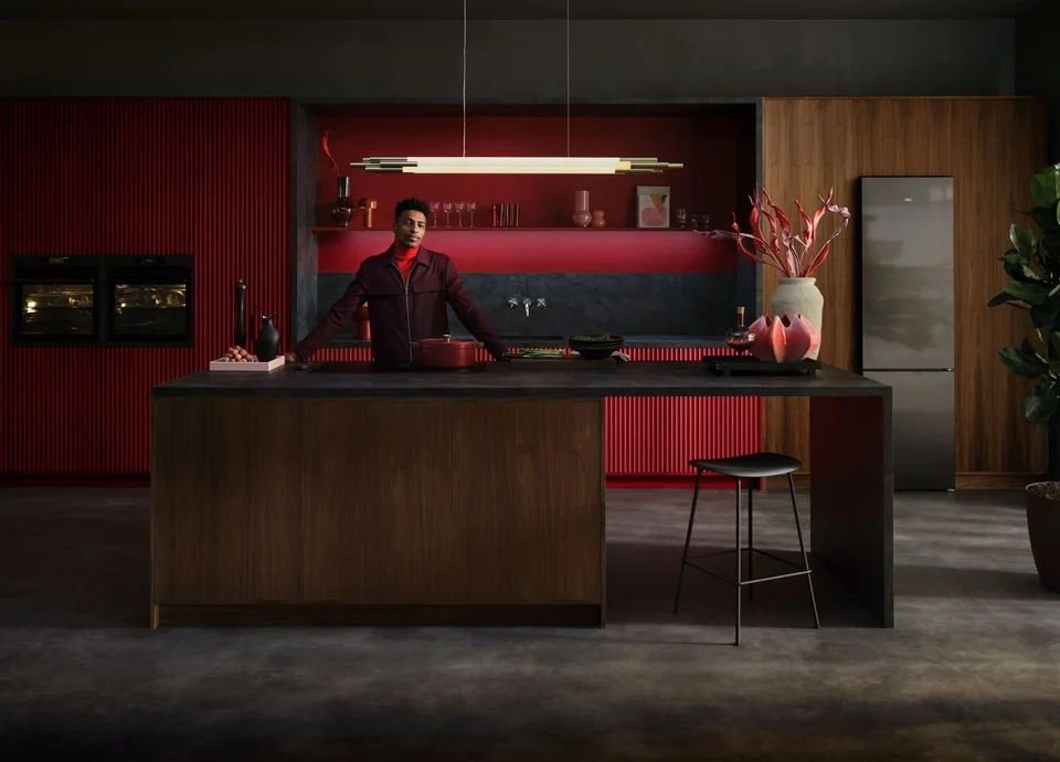 Moderne Küche mit eleganten roten und schwarzen Akzenten, mann steht an einer zentralen Kücheninsel, stilvolle Dekoration und moderne Geräte im Hintergrund.