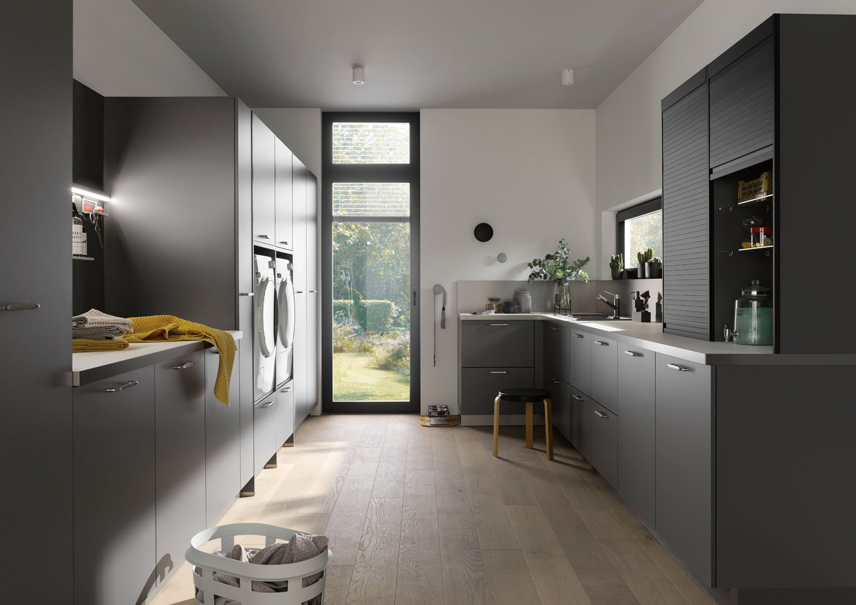 Moderne graue Waschküche mit Waschmaschinen, Trockner, großen Fenstern und Holzboden. Perfekt organisiert und gut belichtet mit eleganten Schränken.