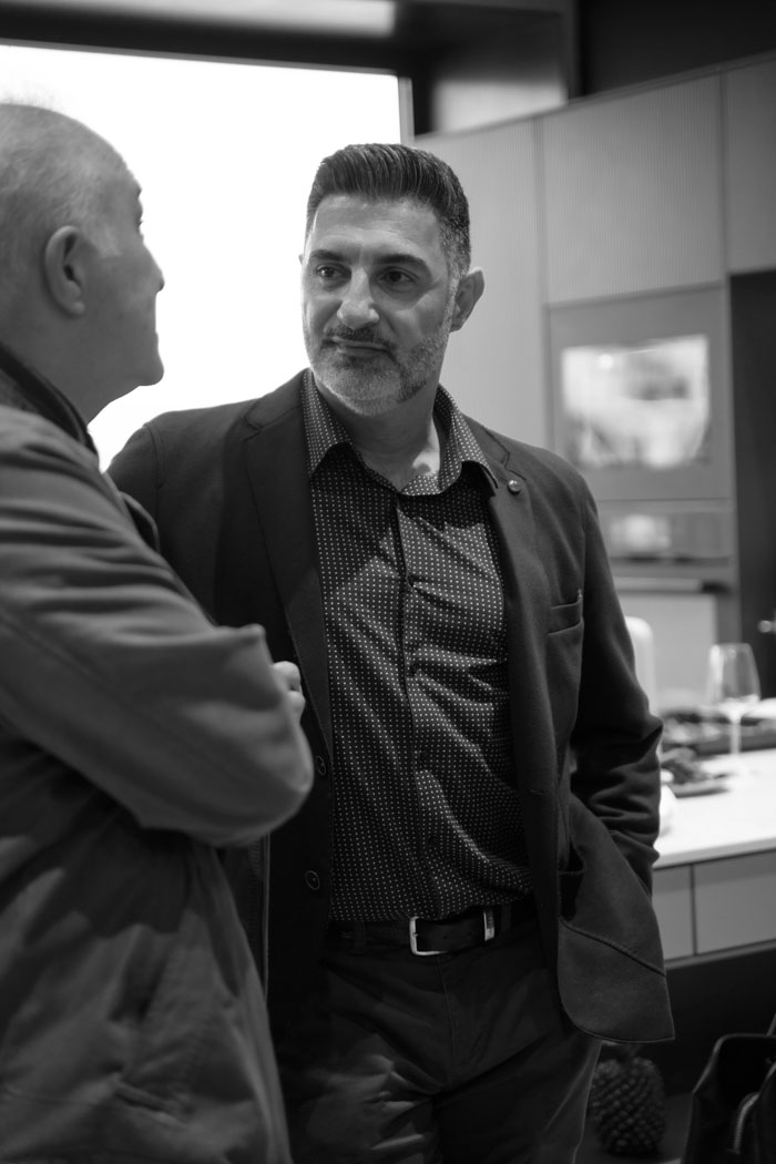 Zwei Männer führen ein Gespräch in einem modernen Raum mit eleganter Einrichtung und einem Tisch im Hintergrund.