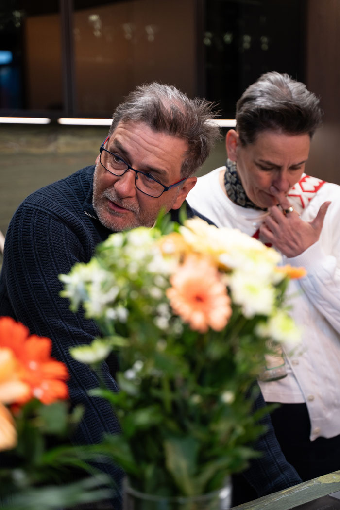 Zwei Personen unterhalten sich in einem modernen Raum, umgeben von bunten Blumenarrangements.