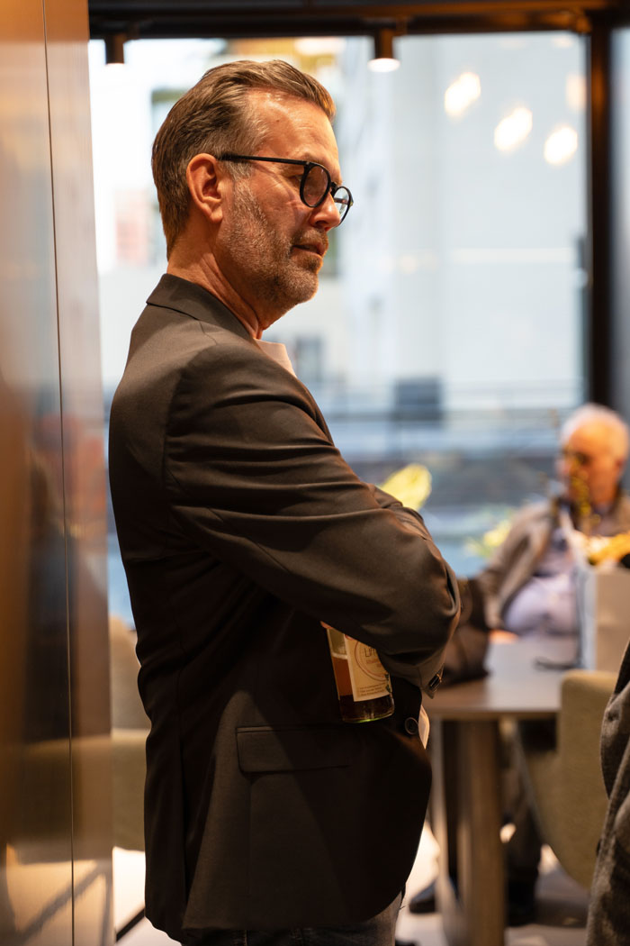 Ein Mann in einem Anzug steht an der Wand und hält eine Flasche in der Hand, während er in einem modernen Raum steht.