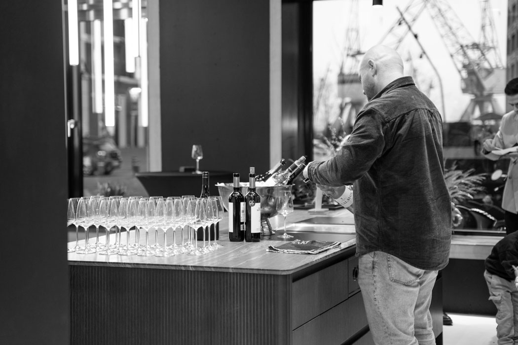 Ein Mann bereitet eine Weinverkostung vor, umgeben von Gläsern und Flaschen in einer eleganten Umgebung.