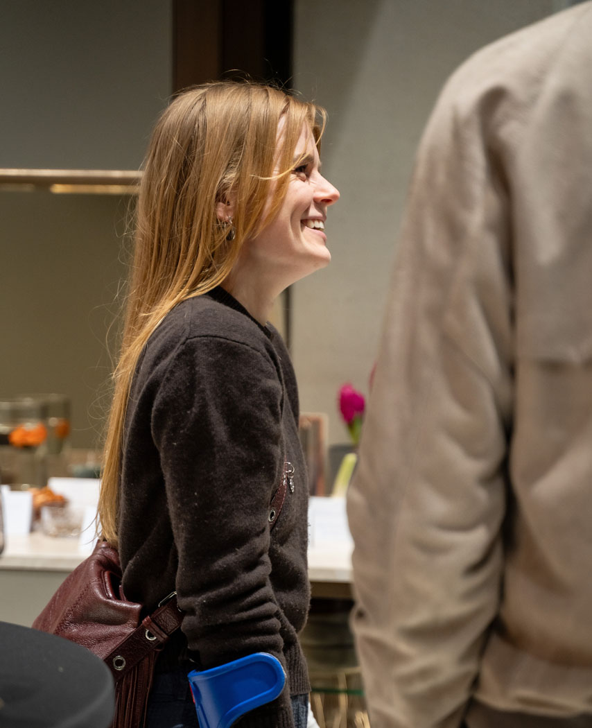 Eine lächelnde Frau mit langen Haaren steht in einer modernen Umgebung und genießt eine Unterhaltung.