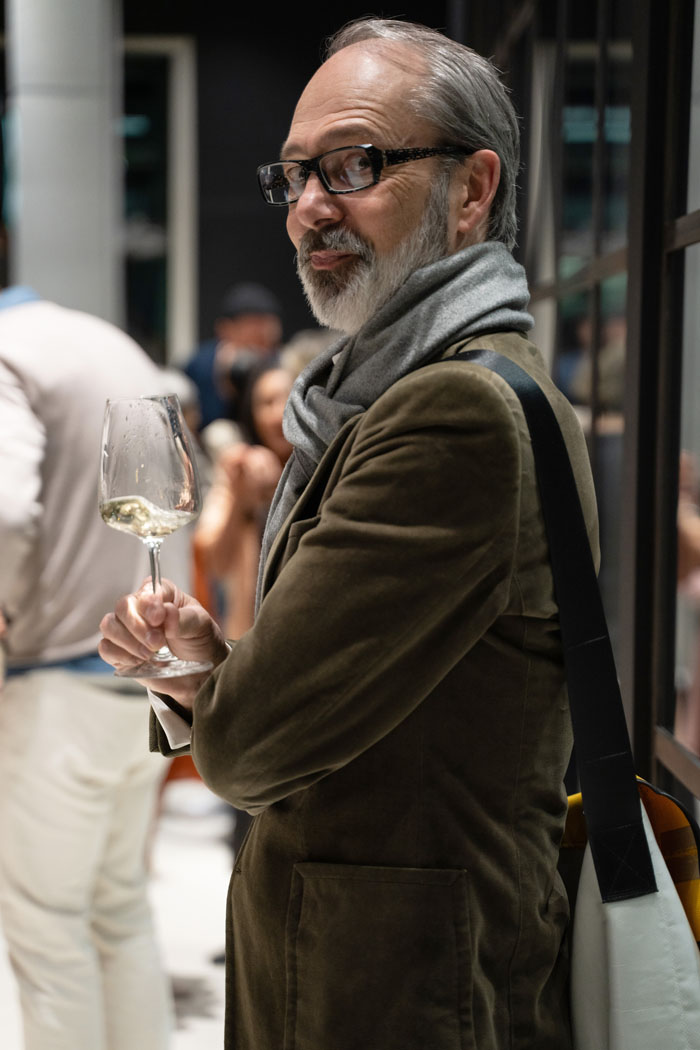 Ein stilvoller Mann mit Brille hält ein Weinglas in einer eleganten Umgebung während einer Veranstaltung.