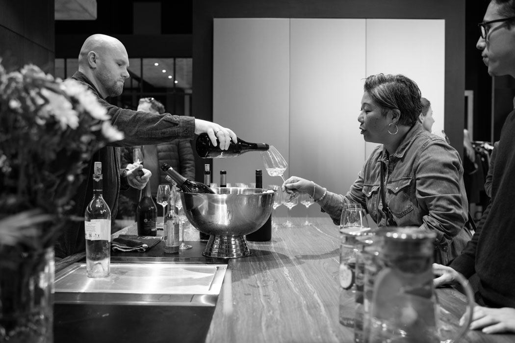 Eine Person schenkt Wein in ein Glas, während eine andere Person aufmerksam zuschaut. Elegante Bar-Atmosphäre.