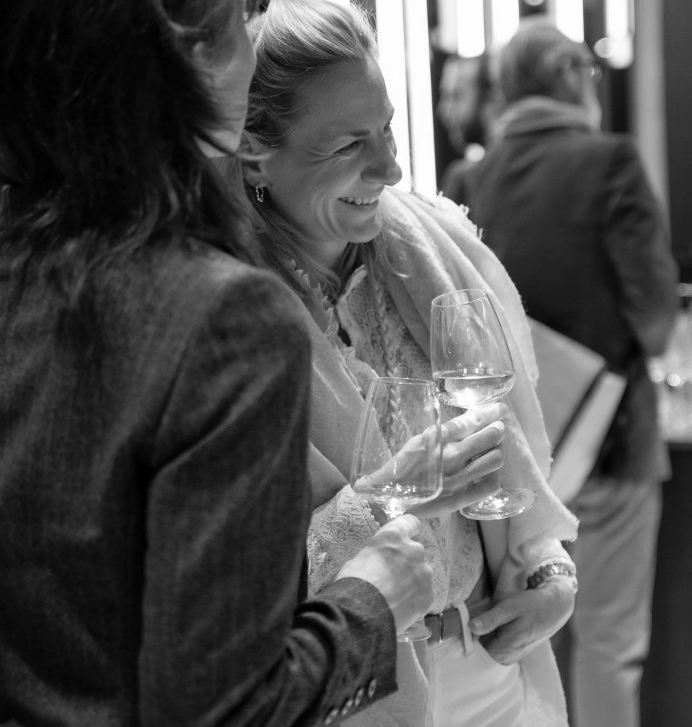 Zwei Frauen halten Weingläser und lachen in einer eleganten Umgebung, die Freude und Geselligkeit ausstrahlt.