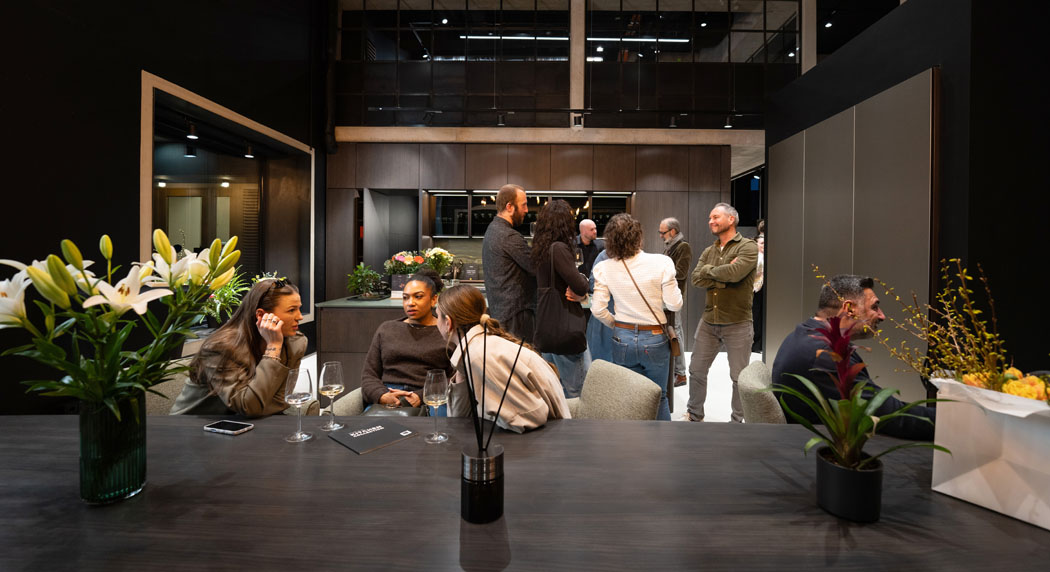 Eine Gruppe von Menschen in einem modernen Raum, die sich unterhalten und Getränke genießen, umgeben von Pflanzen und Blumen.